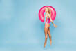 © ViDi Studio - Full body side view young sexy smiling woman wear bikini swimsuit rest near hotel pool hold in hand pink rubber ring jump high isolated on plain blue background. Summer vacation sea sun tan concept.