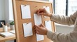 © Arts Eira - Hands pinning blank notes on a cork board, planning and organizing tasks in office