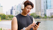 © blueringmedia - Asian Man in Black Tank Top Using Smartphone and Wireless Headphones
