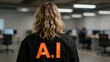 © mihrzn - Back view of a person with wavy blonde hair wearing a black jacket featuring bright orange 'A.I.' text, standing in an office environment with soft focus background.