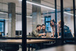© IBEX.Media - Creative startup team collaborating on a laptop in a modern glass office with a robot toy on the desk, viewed through a partition