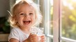 © Rhony - Portrait of little child laughing while holding a glass of water near a sunlit window.