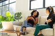 © Wavebreak Media - Female friends sitting and chatting on light-colored sofa in bright living room with open laptop