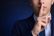 © New Africa - Businessman in suit showing hush gesture on blue background, closeup