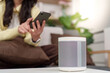 © Natee Meepian - Asian woman using smartphone with smart speaker in modern home