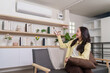 © Natee Meepian - Asian woman using remote control for smart air conditioner at home