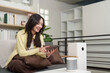 © Natee Meepian - Asian woman using smartphone to control smart home devices, air purifier