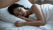 © CrazyJuke - Serene Slumber: A young woman peacefully sleeps in a cozy bed, enveloped by soft white linens and pillows, embodying the tranquility of deep rest.