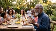 © Oleg - Smiling african american senior man eating dinner at a backyard table with family outdoors. Multigenerational relatives sharing a summer meal together in a garden setting