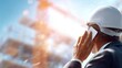 © Premium_art - A male engineer in a white hard hat talks on the phone at a construction site.