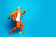© deagreez - Joyful senior man in orange suit dancing and moving energetically against a bright blue background, fashionable active lifestyle portrait conveying confidence, fun and colorful modern style