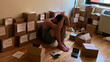 © Дмитрий Лазебный - Tired entrepreneur sits on the floor in a small apartment for an inventory count with stacked product boxes, handwritten labels, and a calculator in realistic documentary style