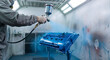 © Vyatcheslav - Worker in protective gear using a spray gun to paint an engine valve cover blue. Automotive mechanic working in an industrial paint booth. Auto body shop repair and maintenance