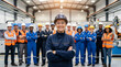 © Rohan Katwe - Confident female supervisor stands with a diverse manufacturing team in a busy industrial factory, all wearing safety gear and high-visibility vests, conveying teamwork, leadership, productivity