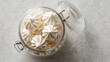 © Chingiz - Sweet, airy meringue cookies sit in a glass jar on a light grey table, seen from above.
