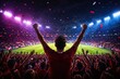 © crispy - Man fan with hands raised cheering at soccer stadium during night match. Excited football supporter celebrating goal with crowd in illuminated arena. Sports victory and emotion concept
