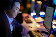 © ultramansk - Excited corporate manager reacting to successful project results on screen. Excited man with headphones working overtime at a desk in a glowing modern workplace at night.