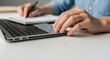 © Tan - Close-up of hands using a laptop and writing in a notebook, symbolizing business and technology in modern work environments