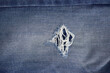 © Maule - Closeup texture of blue denim jeans with a ripped hole and frayed white threads.