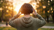 © DN - Young man wearing headphones listening to music in park at sunset