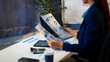 © Phushutter - Businesswoman in office reviewing printed analytics reports with charts and graphs, using tablet and laptop on desk with calculator and coffee.