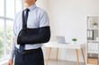 © sukarman - Businessman With Arm Sling Recovering From Injury While Standing in Modern Office