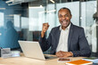 © Liubomir - Confident, older businessman joyfully celebrating an achievement at his office desk, raising a clenched fist in triumph, embodying concepts of victory, pride, and executive power