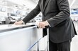 © starush - Businessman at check-in counter holding rolling suitcase in modern airport