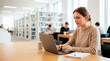 © Xenia - Focused female student using a laptop in a university library. Young woman typing on a computer while studying at a desk. Academic research and online education concept