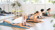 © JackF - Group of women practicing pigeon pose of yoga on black mat in fitness room