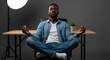 © Wong - Young African man in casual attire meditating peacefully while sitting cross-legged in a modern office workspace