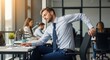 © FARDIN CREATIONS - Man in business attire stretches at his desk in a modern office environment with coworkers working.
