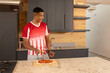 © wavebreak3 - Adult male wearing red-white shirt preparing pizza with cutter on marble island wooden board