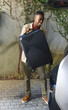 © wavebreak3 - Adult African American man tilting black suitcase preparing to load into open trunk on stone pavers