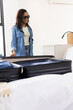 © wavebreak3 - African American woman standing left by bed, unpacking suitcase in denim and sunglasses, copy space
