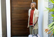 © wavebreak3 - African American man standing at doorway with wheeled suitcase and passport, wearing beige tee