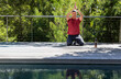 © wavebreak3 - Man kneeling in red shirt, joggers, pressing palms overhead, meditating on deck with water bottle