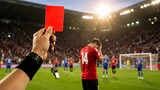 Referee holding a red card up to a soccer player during a professional match in a stadium.