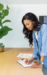 © wavebreak3 - African American woman leaning at desk writing in lined notebook with pen, denim shirt