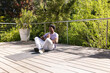 © wavebreak3 - African American man sitting on yoga mat on wooden deck in casual activewear near metal railing
