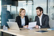 © Liubomir - Two diverse business professionals collaborating during a meeting, discussing important documents and working together on a project in a modern office environment