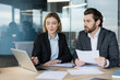 © Liubomir - Business people working together, discussing data and ideas while using a laptop and reviewing documents, showcasing teamwork and professional cooperation in an office setting