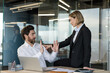 © Liubomir - Businessman reacting uncomfortably, raising hands to stop a confident female coworker sitting on his desk, creating an awkward situation in a corporate workplace