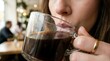 © kurnia - Close-up of a person enjoying a hot beverage, taking a comforting sip of coffee from a clear glass mug indoors
