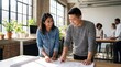 © lahiru - Two colleagues collaborate on architectural plans in a modern office setting with coworkers nearby
