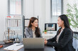 © Kritdanai - Business Consultation: Two professional women in business attire engage in a productive discussion at a modern office, with a laptop, legal scales.