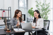 © Kritdanai - Legal Consultation and Partnership: Two smiling professional women engage in a collaborative discussion in a bright office setting, with a laptop and legal documents on the desk.