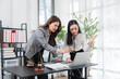 © Kritdanai - Legal Consultation: Two focused female legal professionals collaborate intently at a desk, examining documents and a laptop, discussing a case with determination in a modern office setting.