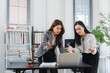 © Kritdanai - Disagreement in the Office: Two businesswomen, with looks of concern and confusion on their faces, gesture emphatically while examining a laptop screen in a modern office setting.