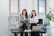 © Kritdanai - Confident Legal Professionals: Two women in professional attire stand confidently with arms crossed in an office setting, surrounded by legal books and a modern desk, exuding competence and authority.